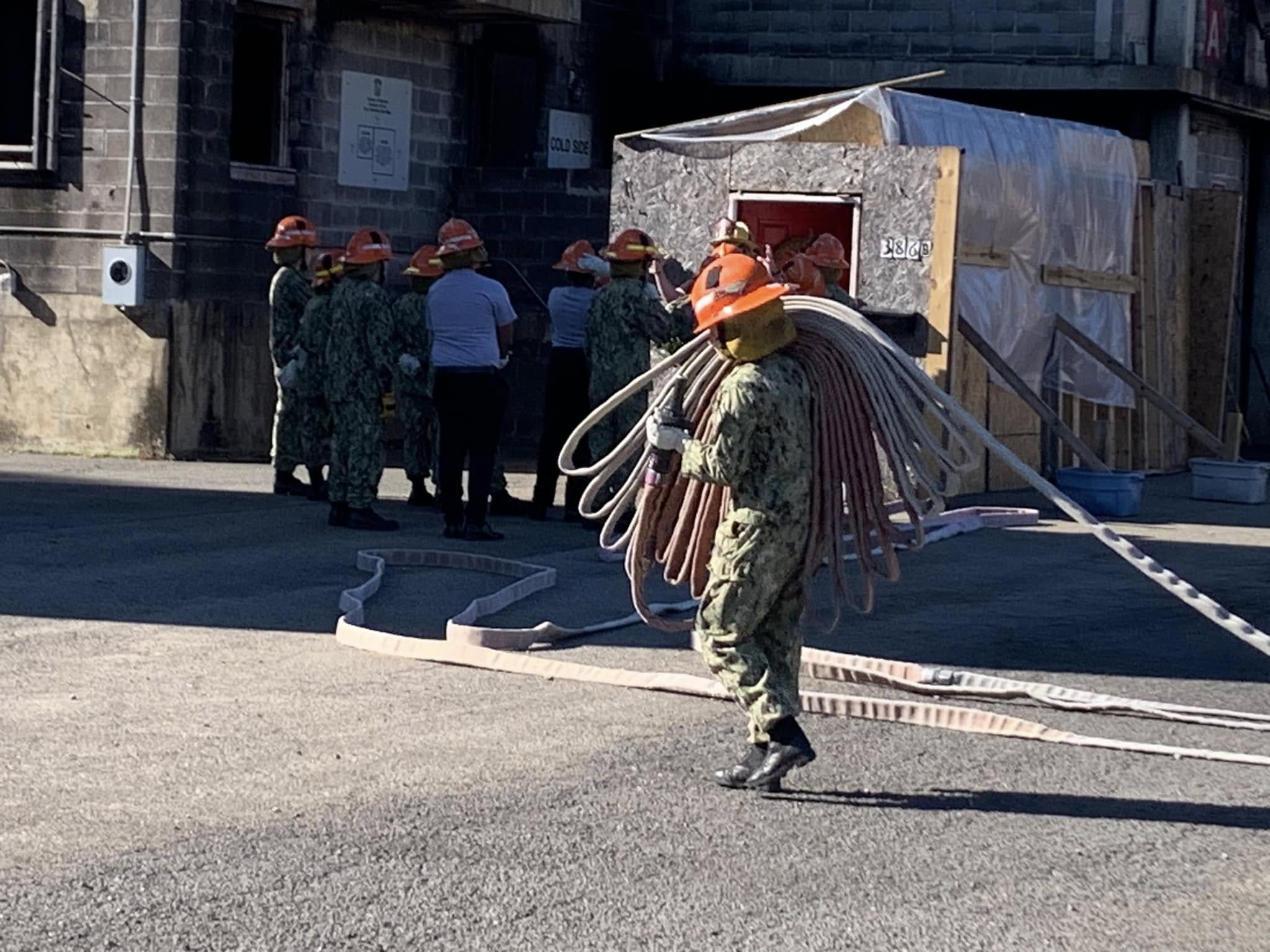 AMERICA Division cadet carrying fire hose coils at a live firefighting training facility