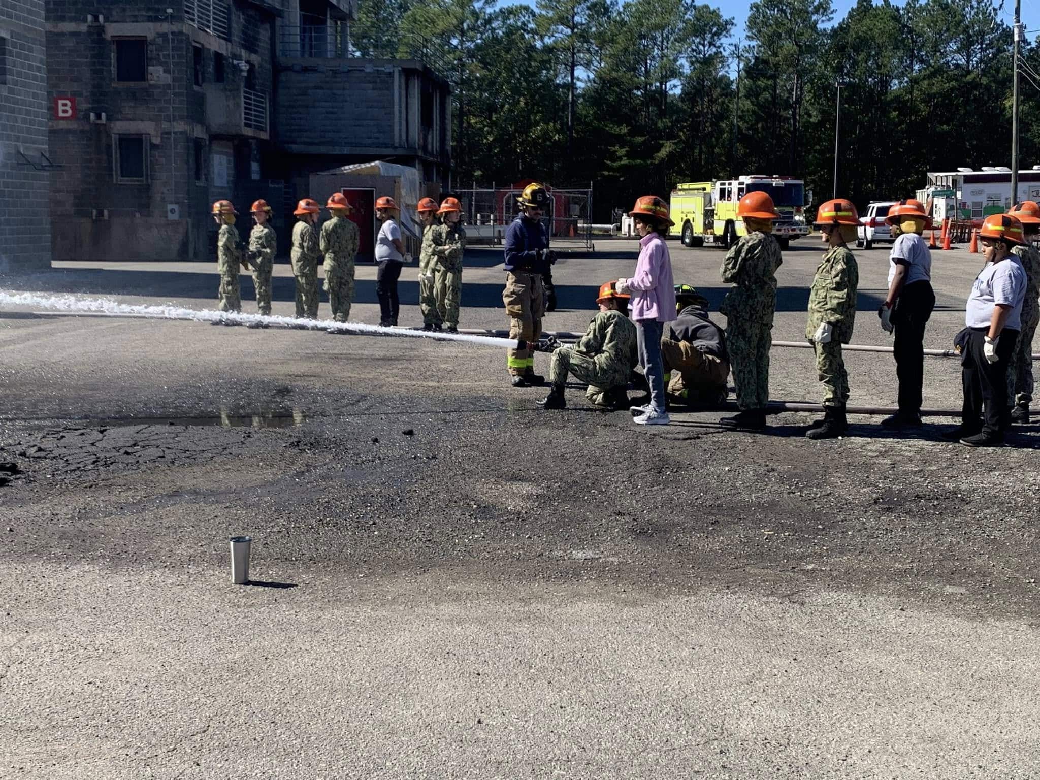 Full group of AMERICA Division cadets in orange helmets at firefighting training facility