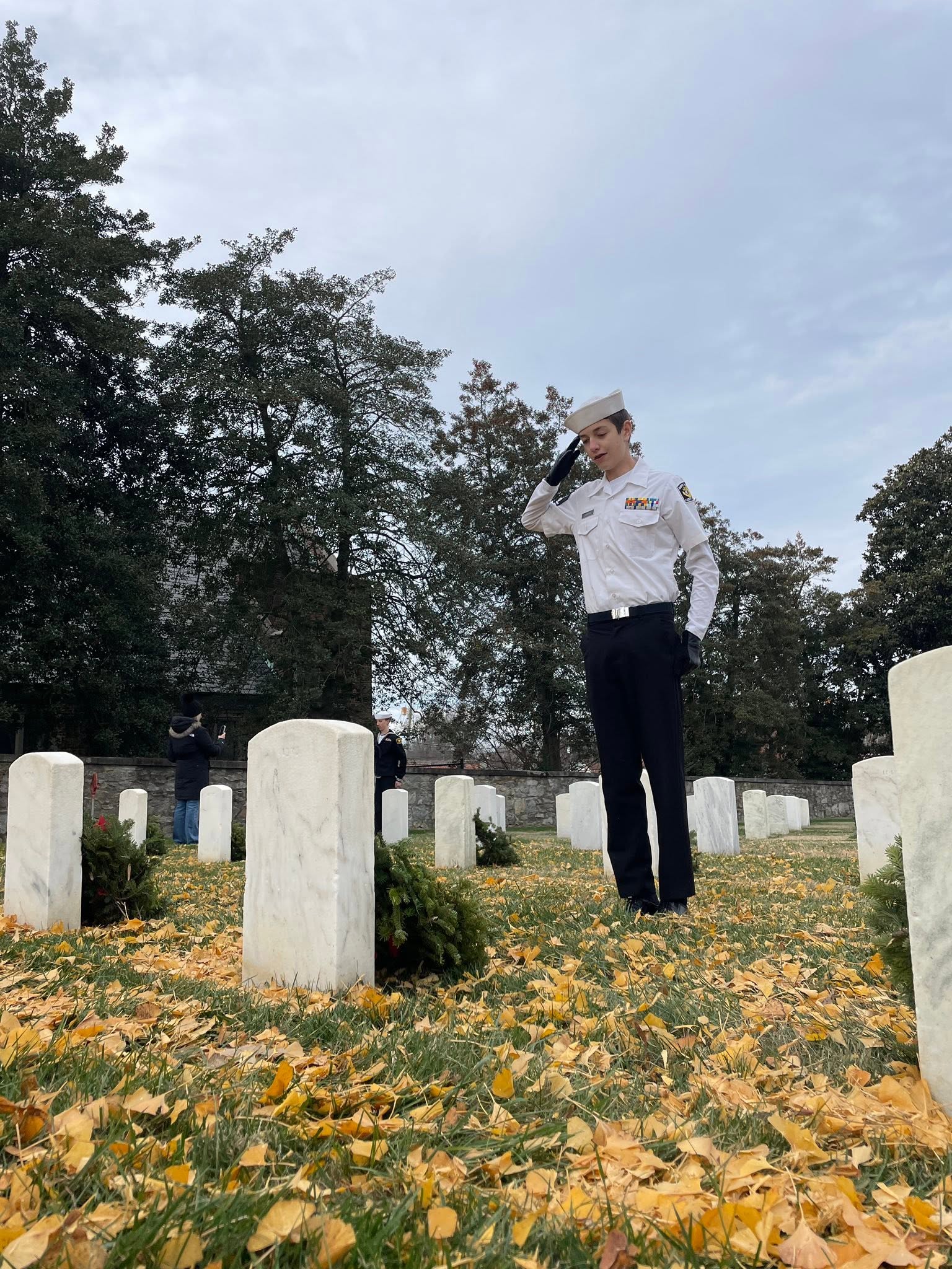 America Division Sea Cadet saluting at a fallen service member's grave during Wreaths Across America at Richmond National Cemetery