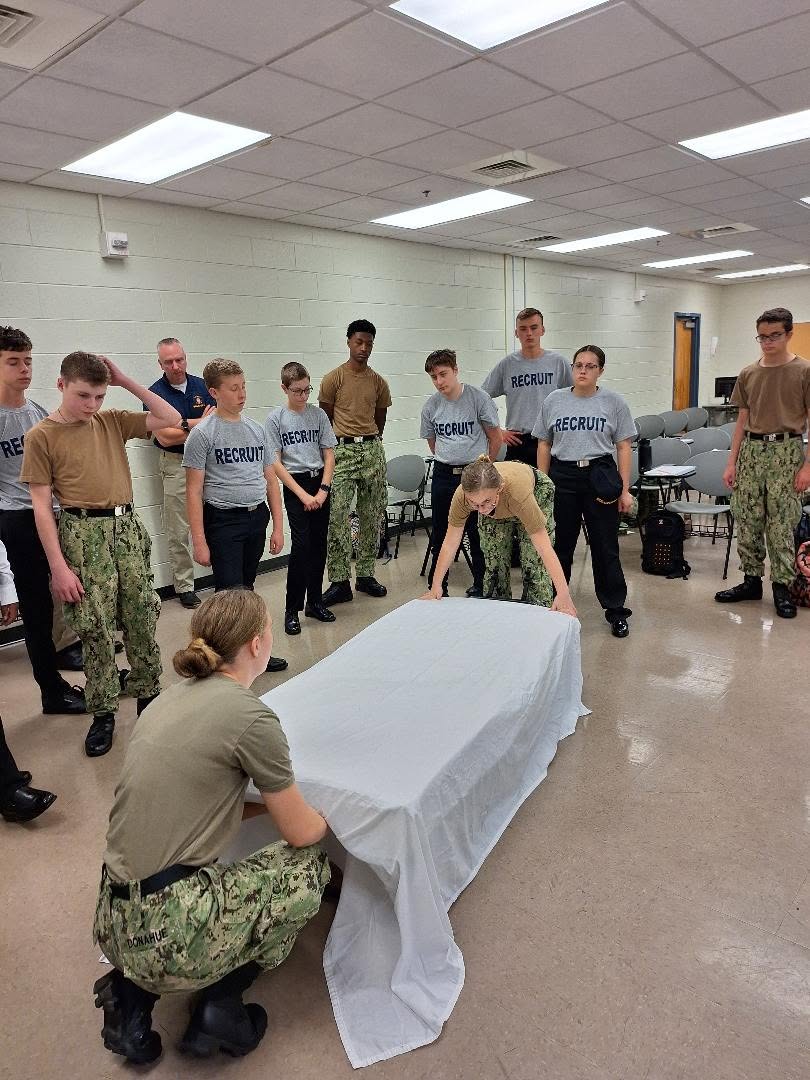Recruits watching an older cadet demonstrate bed-making during orientation