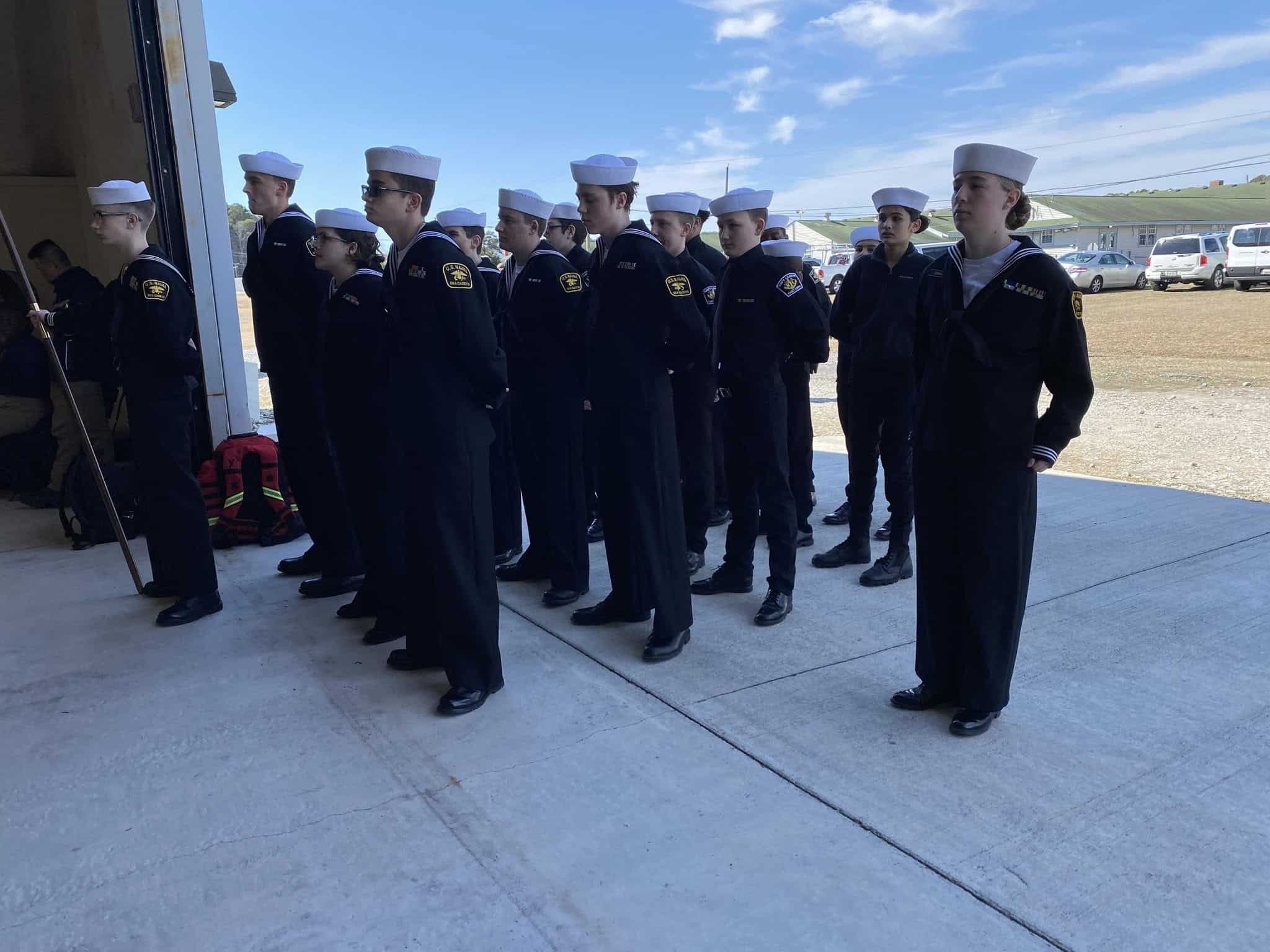 Cadets in dress blues standing in formation outside a fire station