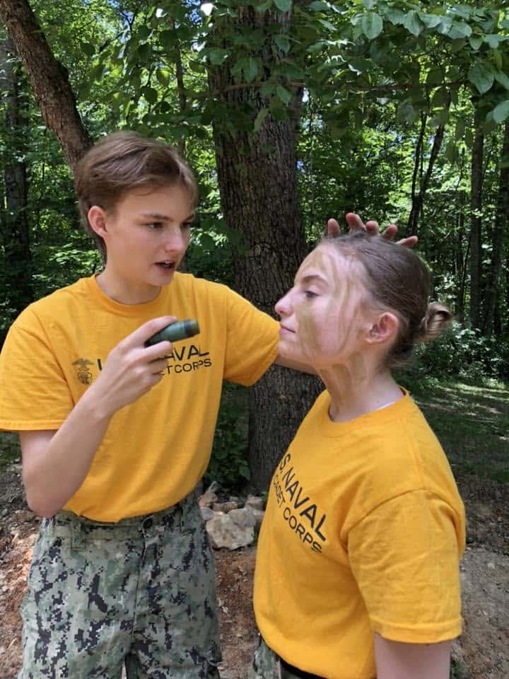 Two cadets applying camo face paint in the woods